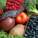 Several fruits and vegetables including raspberries, a tomato, potato, blueberries and broccoli.