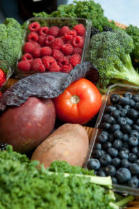 Several fruits and vegetables including raspberries, a tomato, potato, blueberries and broccoli.