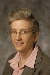 Posed professional headshot photo of a woman wearing a grey blazer, pink shirt and glasses