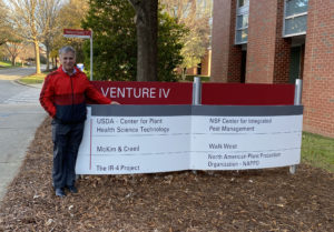 Man wearing black pants and red jacket standing next to a marquee sign in front of a brick building