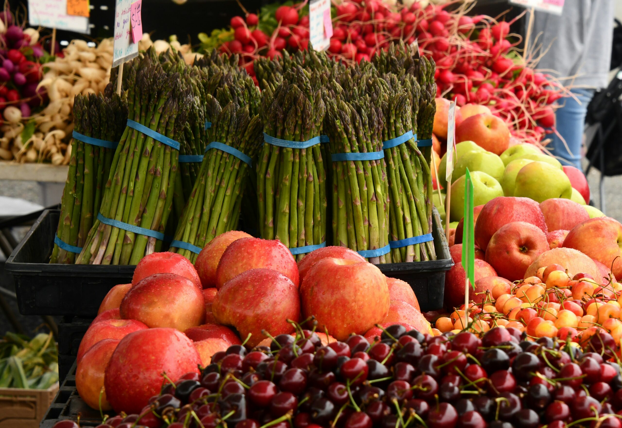 shelley-pauls-G7WdvR8rDPg-unsplash A display of specialty crops at market including asparagus, apples, cherries and radishes.